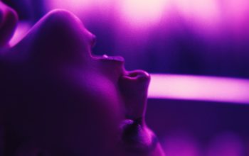 Filmstill zu TOUCH ME. Profilansicht eines Gesichts mit geöffnetem Mund in violettem Licht.